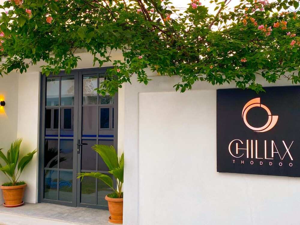 Entrance sign of Chillax Thoddoo surrounded by flowering bushes